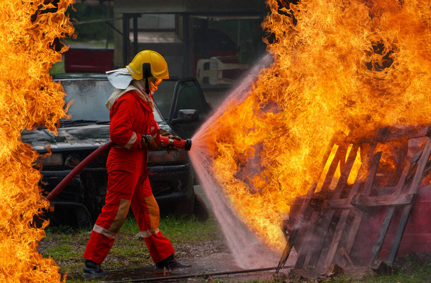Odważny strażak za pomocą gaśnicy i wody z węża do gaszenia pożarów, Strażak opryskujący wodą pod wysokim ciśnieniem do ognia, Szkolenia strażackieTrening strażacki z niebezpiecznymi płomieniami-Image - Zdjęcie, obraz