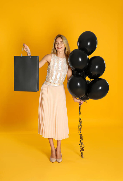 Happy young woman with balloons and shopping bag on yellow background. Black Friday Sale - Foto, Imagem