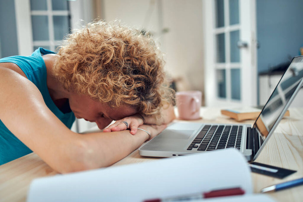 Frau, die zu Hause auf ihrem Schreibtisch schläft, während sie aus der Ferne freiberuflich arbeitet. Moderne Probleme und Probleme bei der Arbeit von zu Hause aus. - Foto, Bild