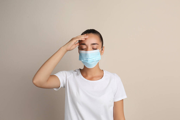 Stressed woman in protective mask on beige background. Mental health problems during COVID-19 pandemic - Фото, зображення