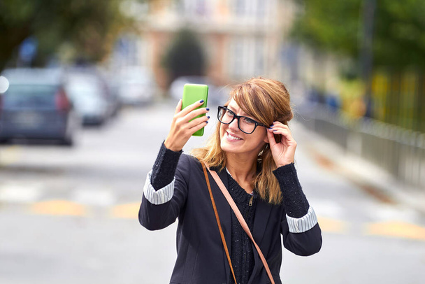 Cute young caucasian woman holding modern smartphone on the street. - Fotó, kép