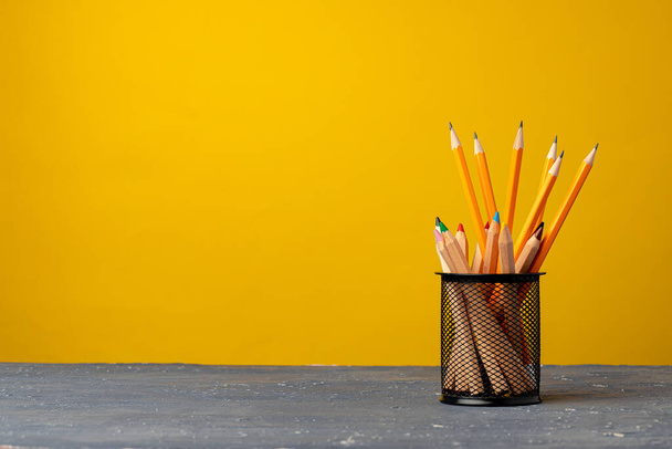 Office cup with pencils and stationery against yellow background - Foto, afbeelding