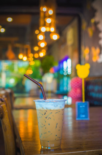 Eiskaffee in Plastikbecher auf Holztisch mit Bokeh-Hintergrund. - Foto, Bild