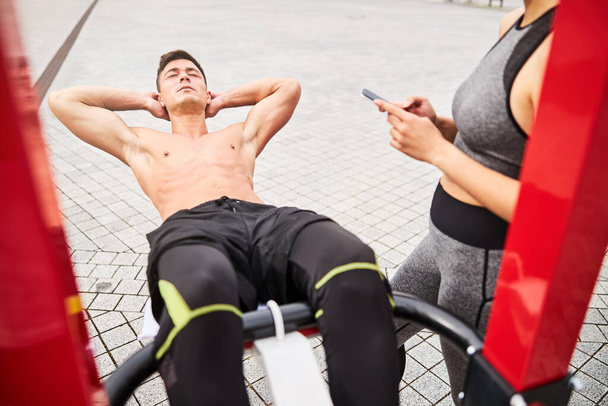 Мускулистый человек тренировки брюшной полости с подругой поддержки на открытом воздухе - Фото, изображение