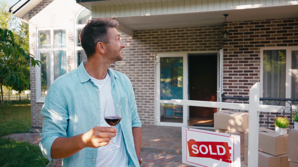 Χαρούμενος άντρας κρατώντας ένα ποτήρι κρασί και κοιτάζοντας το νέο σπίτι  - Πλάνα, βίντεο