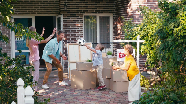 mãe jogando futebol para crianças perto do marido, caixas de papelão e nova casa - Filmagem, Vídeo