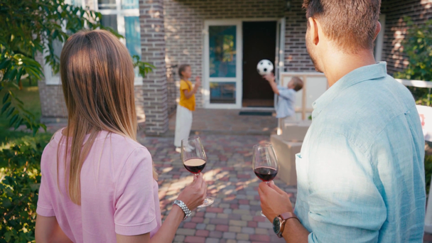 enfoque selectivo de pareja sosteniendo copas de vino cerca de los niños y la nueva casa - Imágenes, Vídeo