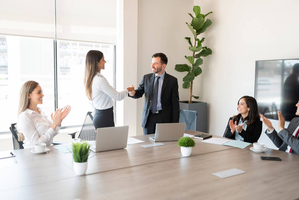 Uomo d'affari che stringe la mano a una collega in ufficio mentre altri colleghi li applaudono durante una riunione - Foto, immagini