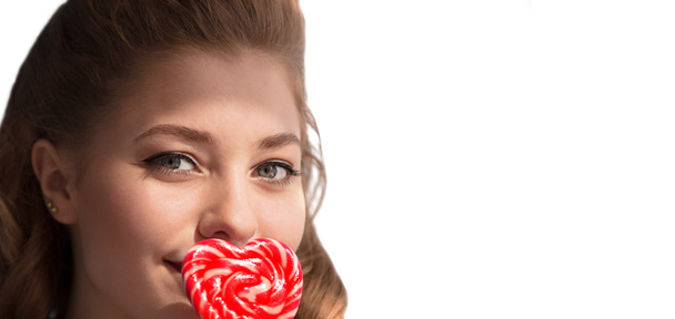 La cara de una chica con caramelos en un palo en forma de corazón sobre un fondo blanco. Dulce mujer. - Foto, imagen