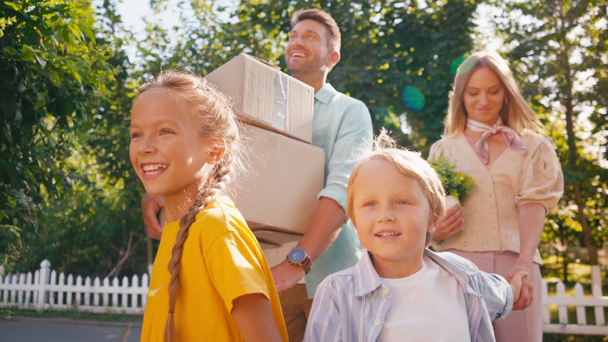 padres sosteniendo cajas y plantas mientras caminan con los niños, concepto de reubicación - Imágenes, Vídeo