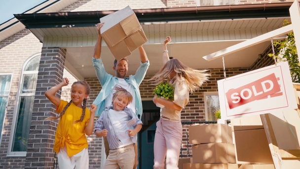 Kinder und Eltern tanzen vor neuem Haus und verkaufen Brett  - Filmmaterial, Video