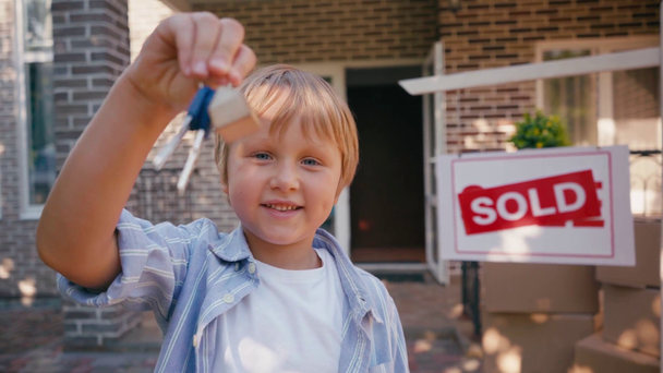 Aufgeregter Junge hält Schlüssel in der Nähe von verkauftem Brett und neuem Haus  - Filmmaterial, Video