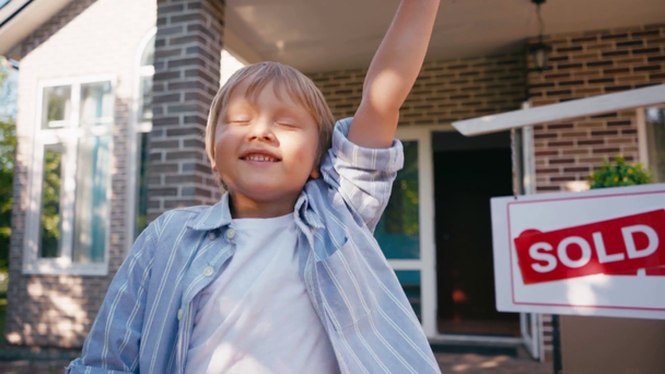 chico emocionado sosteniendo las llaves y saltando cerca de tablero vendido y casa nueva  - Metraje, vídeo