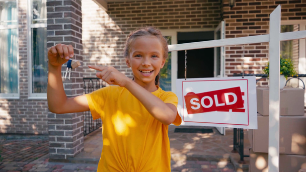 niño alegre señalando con el dedo las llaves cerca de la nueva casa - Metraje, vídeo