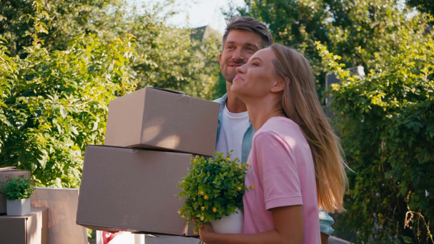 Man en vrouw wandelen met kartonnen dozen en planten, verhuisconcept  - Video