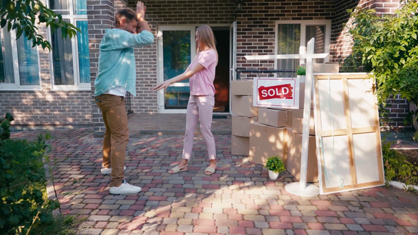 vreugdevol paar geven high five en springen in de buurt van nieuw huis en verkocht boord  - Video