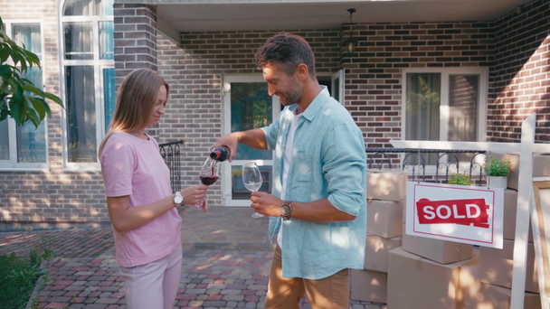 Mann schenkt Frau Wein in Glas in der Nähe von verkauftem Vorstand und neuem Haus ein - Filmmaterial, Video
