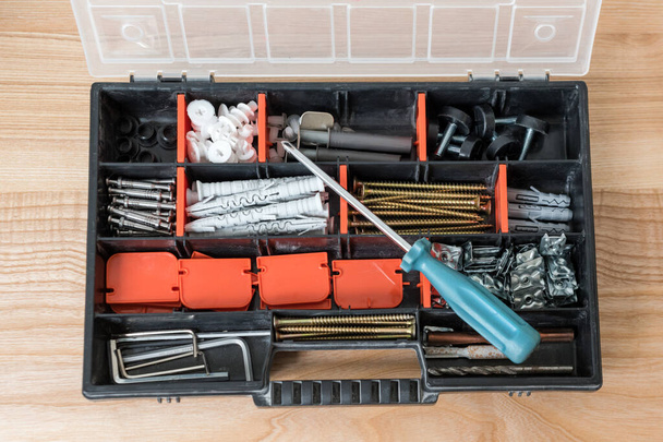 Werkzeugkiste mit verschiedenen Instrumenten öffnen. Schrauben und Schraubendreher Kunststoffbox mit Werkzeug auf Holzgrund. Konzept für Möbelmontage und Renovierung - Foto, Bild