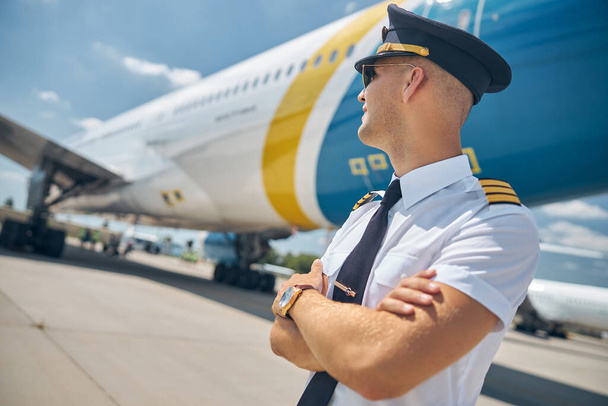 Jóképű férfi pilóta áll repülővel a repülőtéren - Fotó, kép
