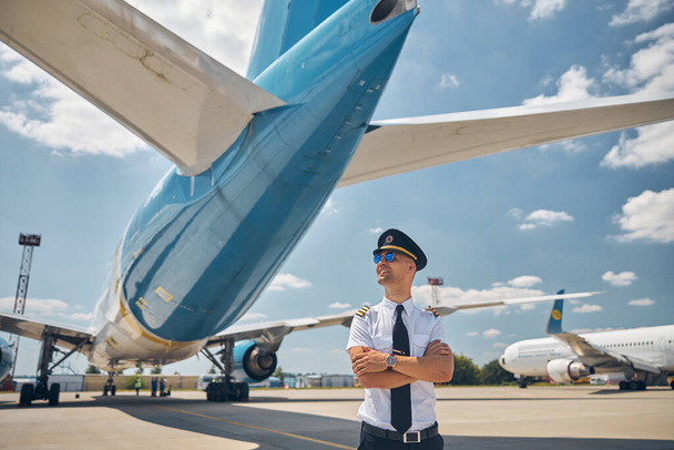 Fröhlicher männlicher Pilot mit Sonnenbrille steht draußen auf dem Flugplatz - Foto, Bild