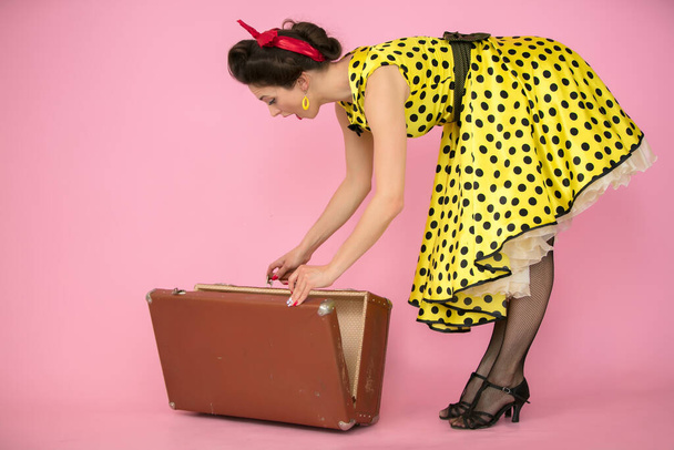 Retro dziewczyna otwiera starą walizkę na różowym tle. - Zdjęcie, obraz