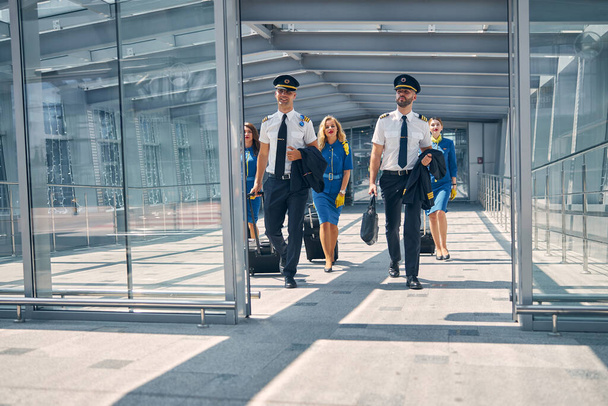 Екіпаж з пересувними валізами, що ходять в терміналі аеропорту
 - Фото, зображення