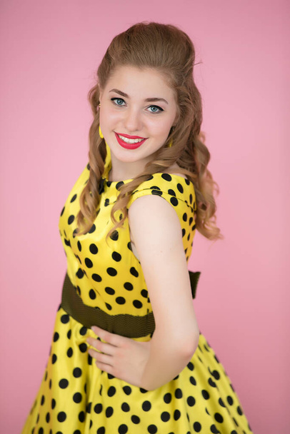 Portrait of a retro girl. Woman in a yellow dress on a pink background. - Photo, Image