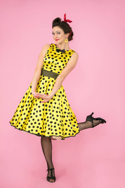 Retro girl. Beautiful woman in a dress with polka dots on heels on a bright background. - Photo, Image