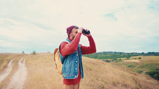 Reisender mit Rucksack blickt durch Fernglas, steht auf Hügel - Filmmaterial, Video