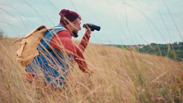Boční pohled na cestovatele sedícího a hledícího dalekohledem na trávu - Záběry, video