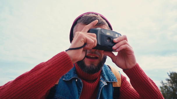 Podróżnik z plecakiem robiący zdjęcia z zabytkową kamerą na zewnątrz - Materiał filmowy, wideo
