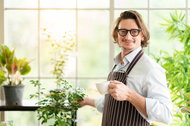 幸せとリラックスして趣味をしている男は、コーヒーを飲みながら温室の庭の農場で木の植物を見て楽しむ - 写真・画像