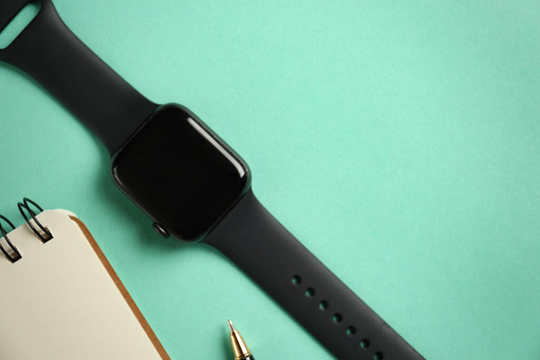 Stylish smart watch and notebook on turquoise background, flat lay. Space for text - 写真・画像
