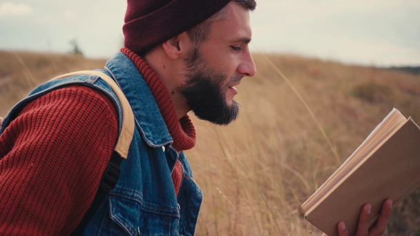 Widok z boku książki podróżnika i siedzi na trawie - Materiał filmowy, wideo