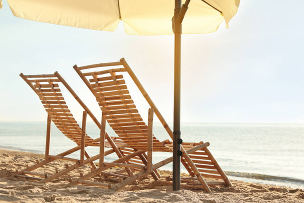 Wooden deck chairs and outdoor umbrella on sandy beach. Summer vacation - Fotografie, Obrázek