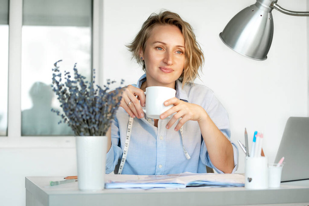 Eine junge Arbeiterin macht Pause, trinkt Tee am gemütlichen Büroarbeitsplatz. Fernarbeit, E-Learning-Konzept, Online-Studium, Business - Foto, Bild