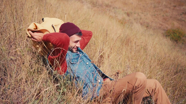 Widok z boku podróżnika siedzącego i leżącego na plecaku na wzgórzu - Materiał filmowy, wideo