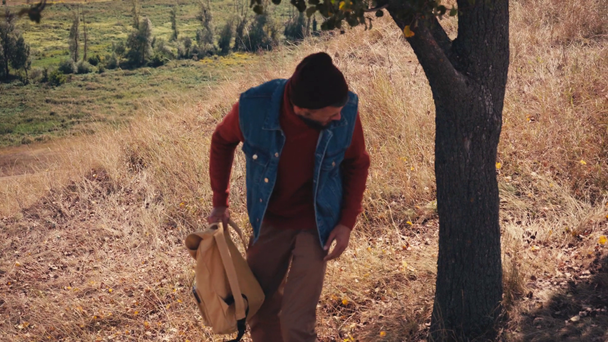Turista con mochila bajando y apoyándose en el árbol - Imágenes, Vídeo