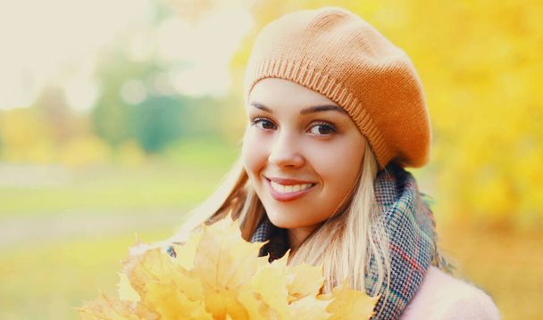 Portrait of beautiful smiling blonde woman with yellow maple leaves in autumn park wearing beret - Фото, зображення