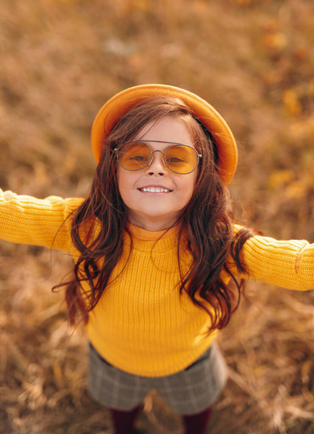 Joyful little girl in trendy clothes standing in field - Foto, imagen