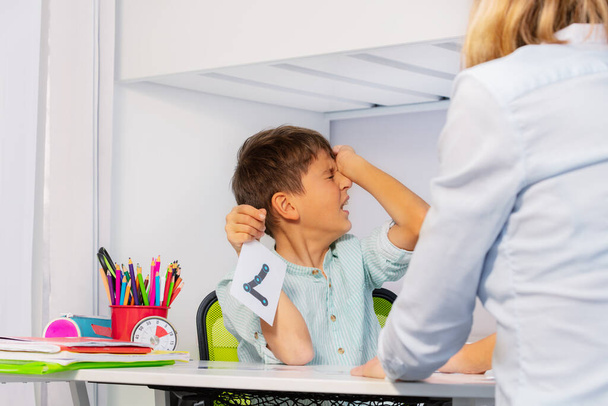 Boy with autism spectrum disorder show pain and negative expression while learning numbers sitting by teacher - Zdjęcie, obraz