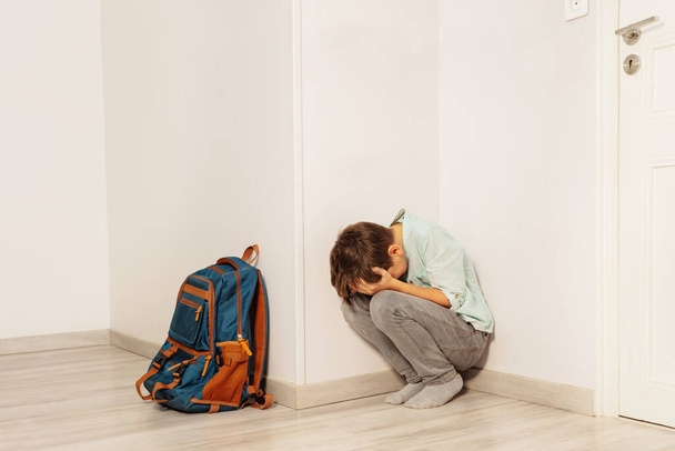 Sad stressed boy bullied in school cry sitting in the corner with son rucksack - Фото, зображення