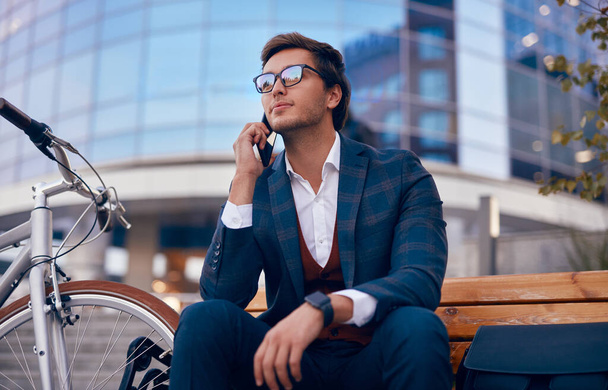 Male entrepreneur speaking on smartphone on bench - Valokuva, kuva