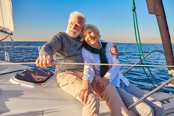 Szczęśliwy piękny starszy rodziny para przytulanie i uśmiech podczas relaksu na żaglówce lub pokładzie jachtu pływających w spokojnym błękitnym morzu, ciesząc się niesamowity widok - Zdjęcie, obraz