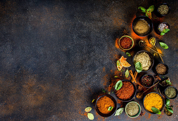Set of Spices and herbs for cooking. Small bowls with colorful  seasonings and spices - basil, pepper, saffron, salt, paprika, turmeric. On black stone table top view copy space - Photo, Image