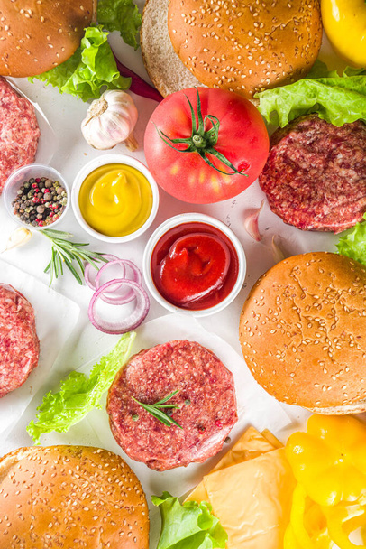 Hamburger arka planı. Çeşitli cheeseburger ve sığır burger malzemelerini hazırla - çörek, domates, soğan, marul, sos, peynir ve çiğ burger pirzolası, ızgara için hazır. Burger bbq parti festivali konsepti, üst görünüm kopyalama alanı - Fotoğraf, Görsel