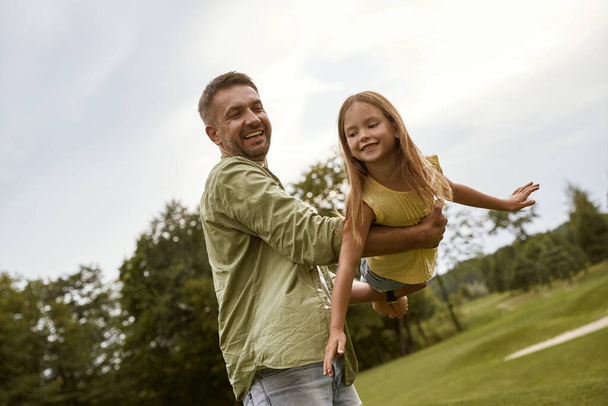 Szczęśliwy ojciec i jego córeczka bawią się w parku w ciepły letni dzień, uśmiechają się i czują się tak szczęśliwi spędzając razem czas - Zdjęcie, obraz
