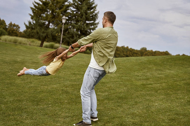 Nuori rakastava isä leikkii ja pitää hauskaa suloisen pienen tyttärensä kanssa vieraillessaan kauniissa vihreässä puistossa lämpimänä kesäpäivänä. - Valokuva, kuva