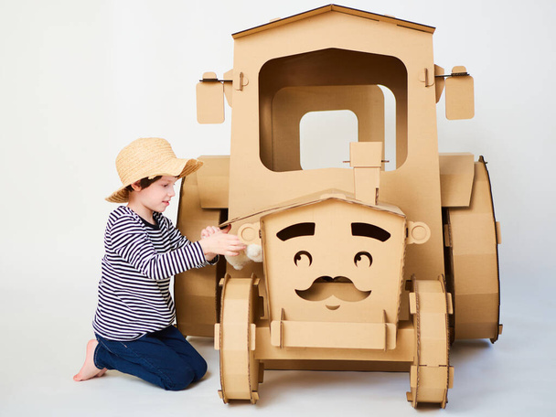 A little boy is playing with cardboard tractor on a white background. Agriculture concept. Mockup for design with copy space. - Zdjęcie, obraz