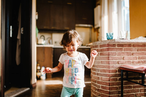 Funny toddler girl dancing indoors, little child play, baby having fun moving and jumping on the floor in a sunny white room, kitchen at home or kindergarten. - Foto, immagini